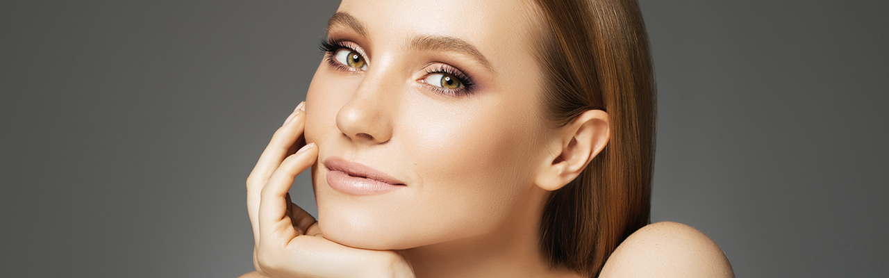 A cropped headshot of beautiful red haired woman with hazel eyes posing with her hand on her chin with a beautifuly shaped nose, symbolizing what a rhinoplasty nose surgery can achieve.