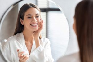 Beautiful woman with a good complexion admires her glowing skin in a bathroom mirror.